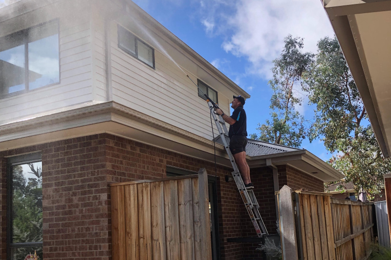Man on ladder pressure cleaning house